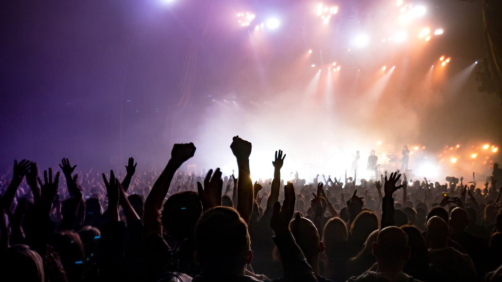 Concert crowd with raised hands facing a brightly lit stage